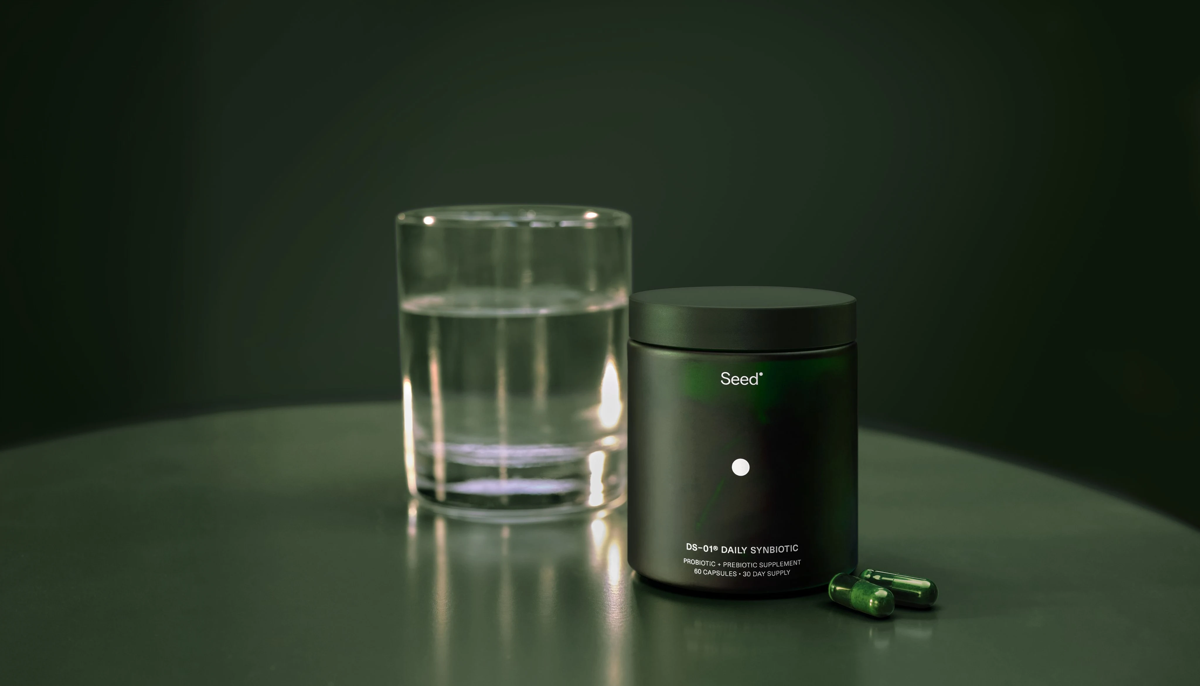 DS-01 Daily Synbiotic jar and capsules beside a glass of water